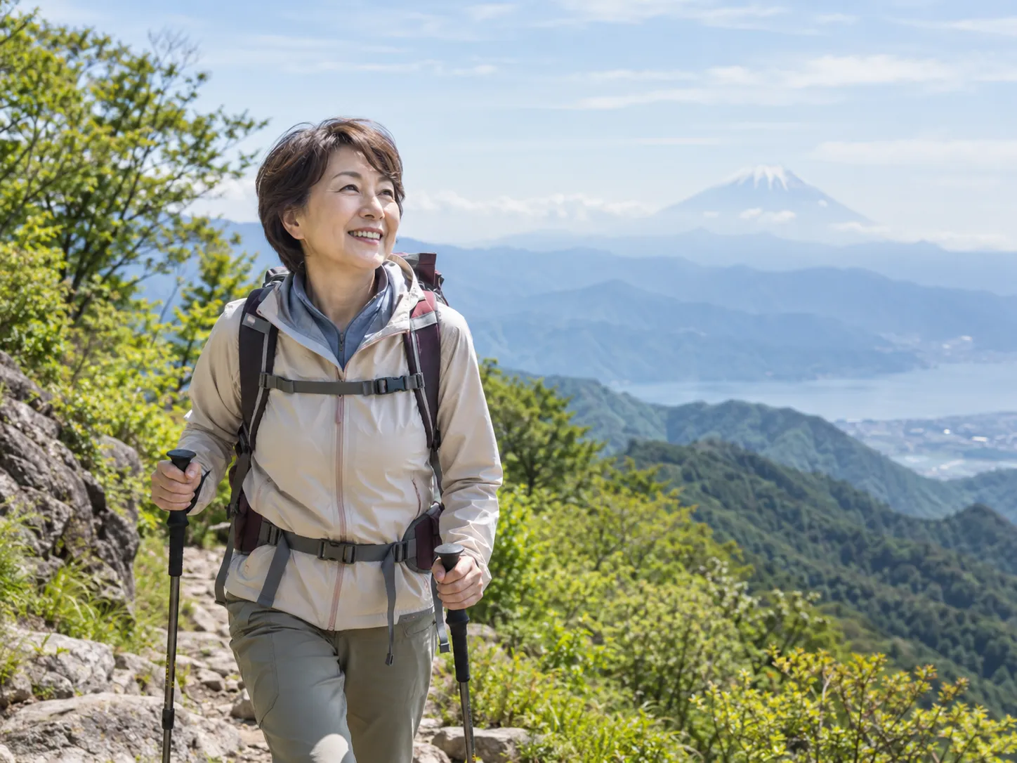 山の景色を眺めながら、笑顔で登山を楽しむ女性。
